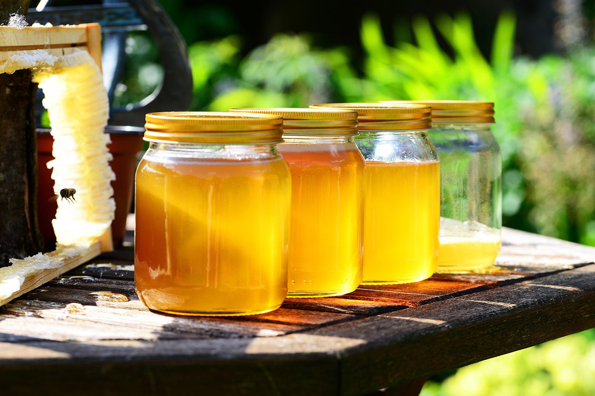 Stół z 4 słoikami miodu, w tle ogród.